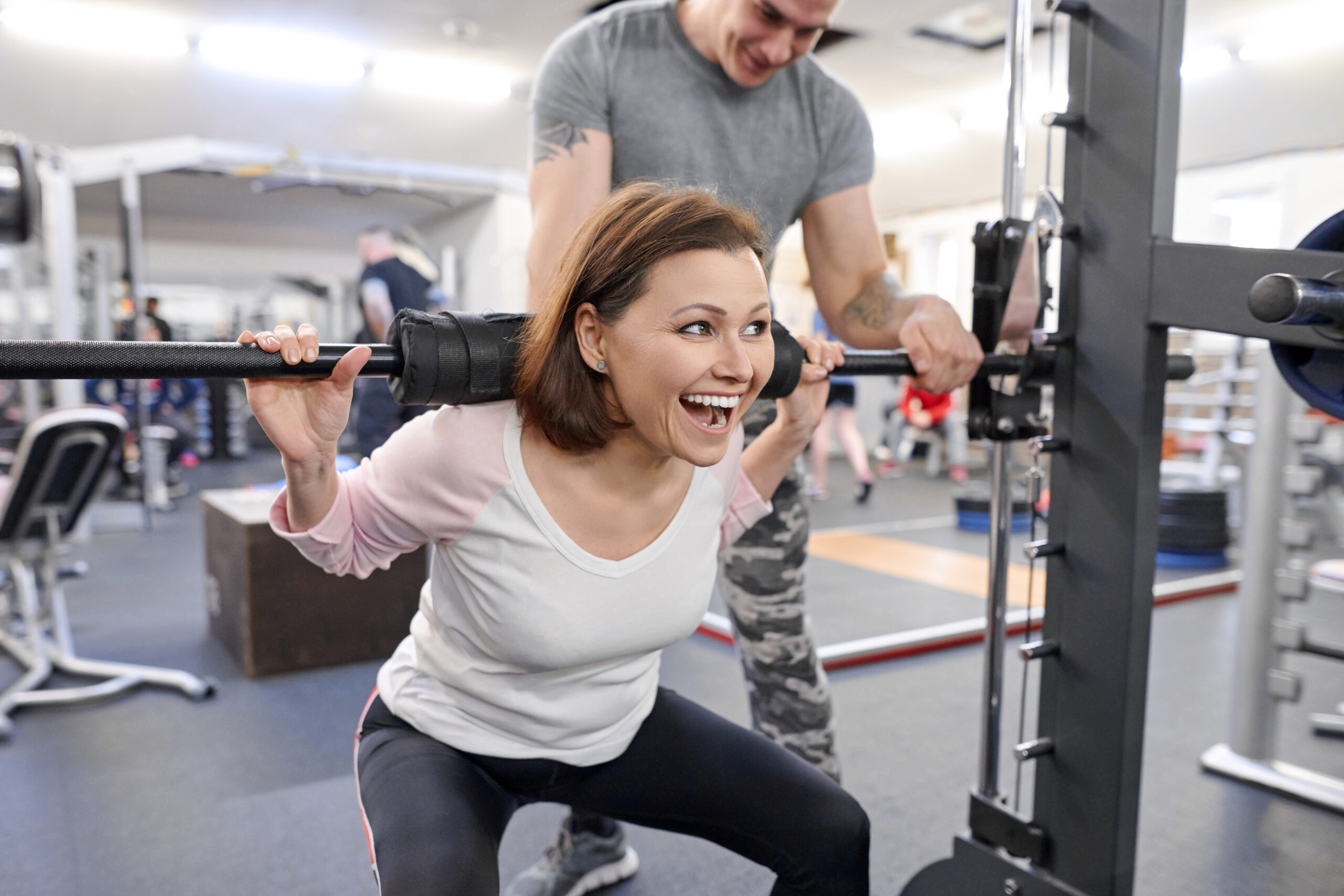Middle-aged woman doing sports exercise in fitness center. Personal gym trainer assisting mature woman. Health fitness sport age concept
