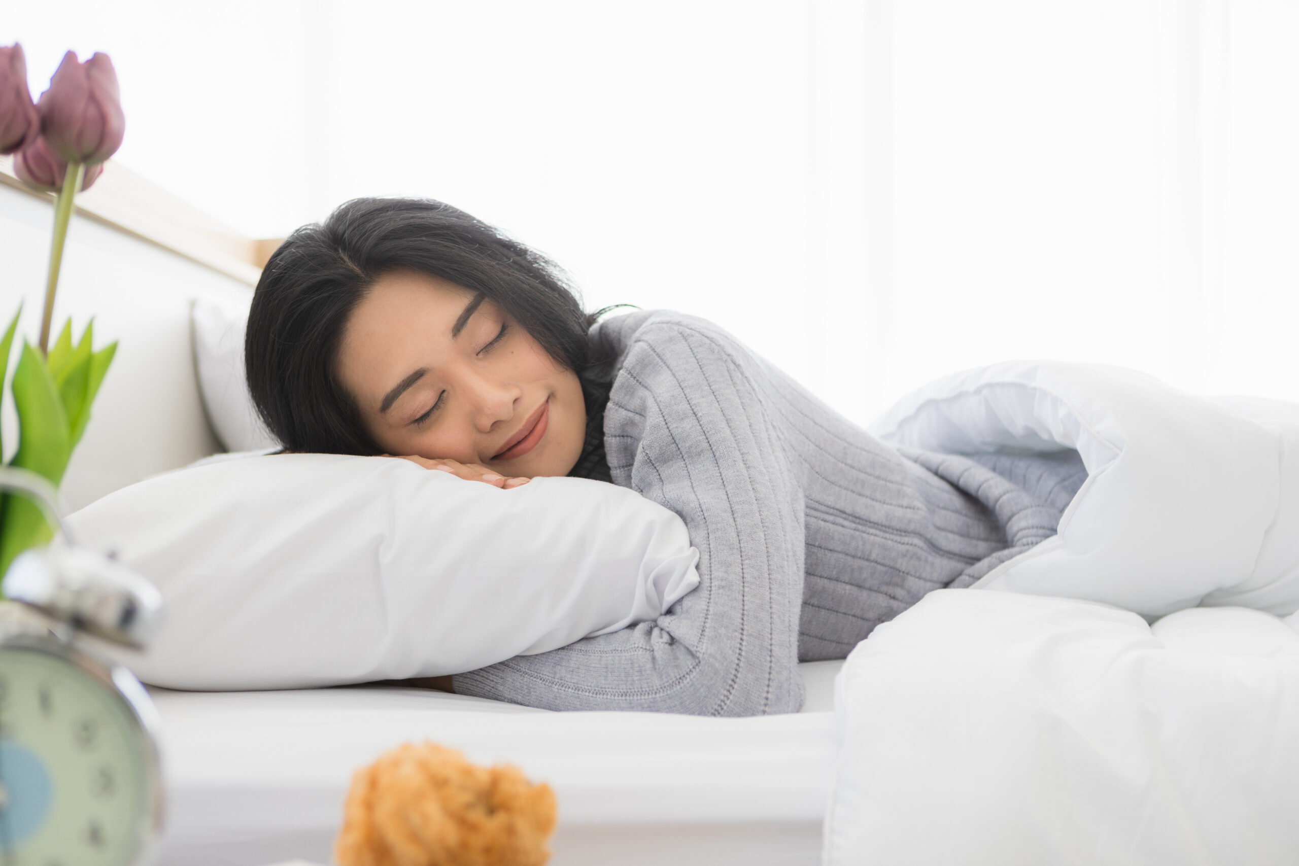 Asian woman lies on one’s side on bed in bedroom.