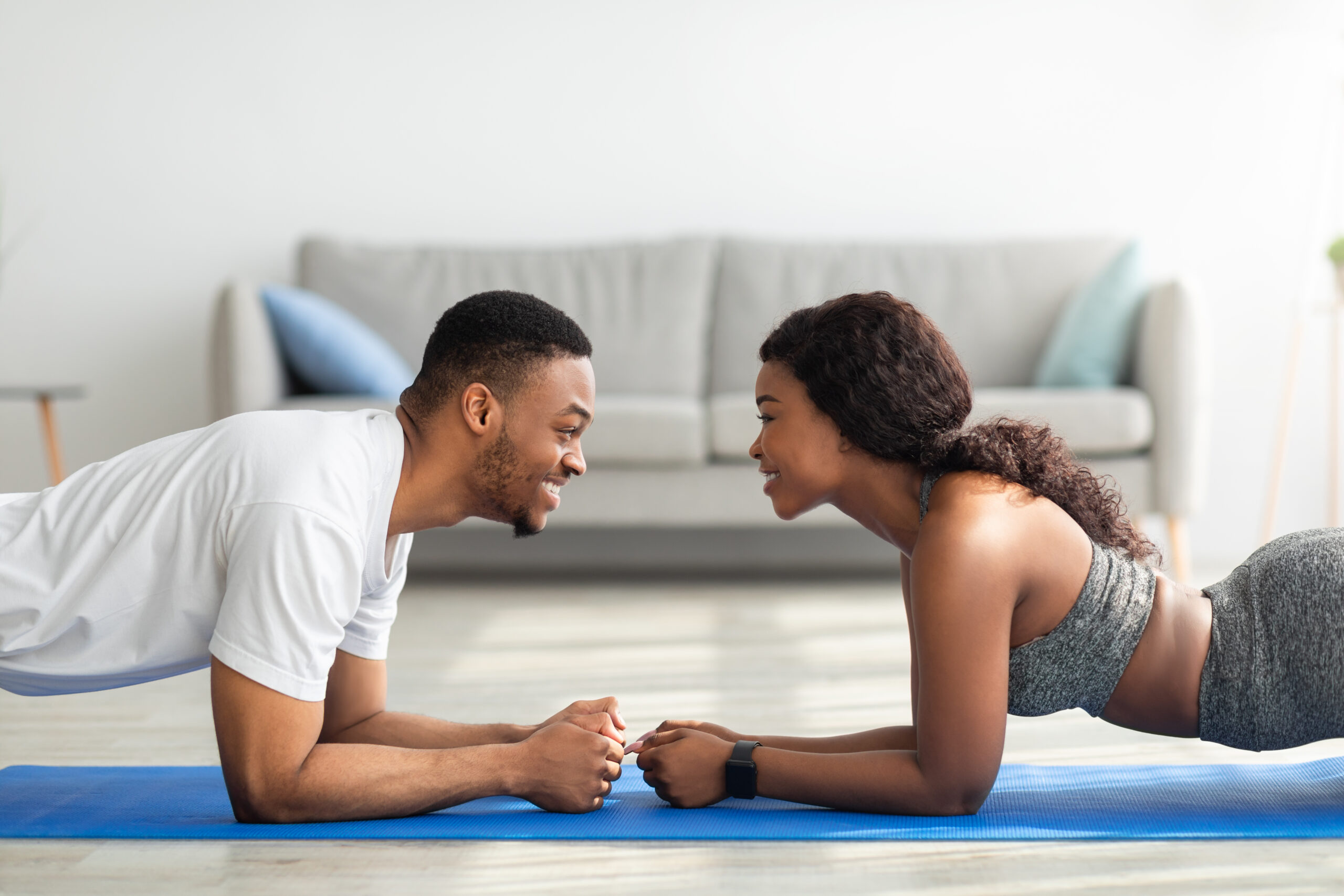 Side view of black couple standing in elbow plank, facing each other, having fun while doing domestic strength workout