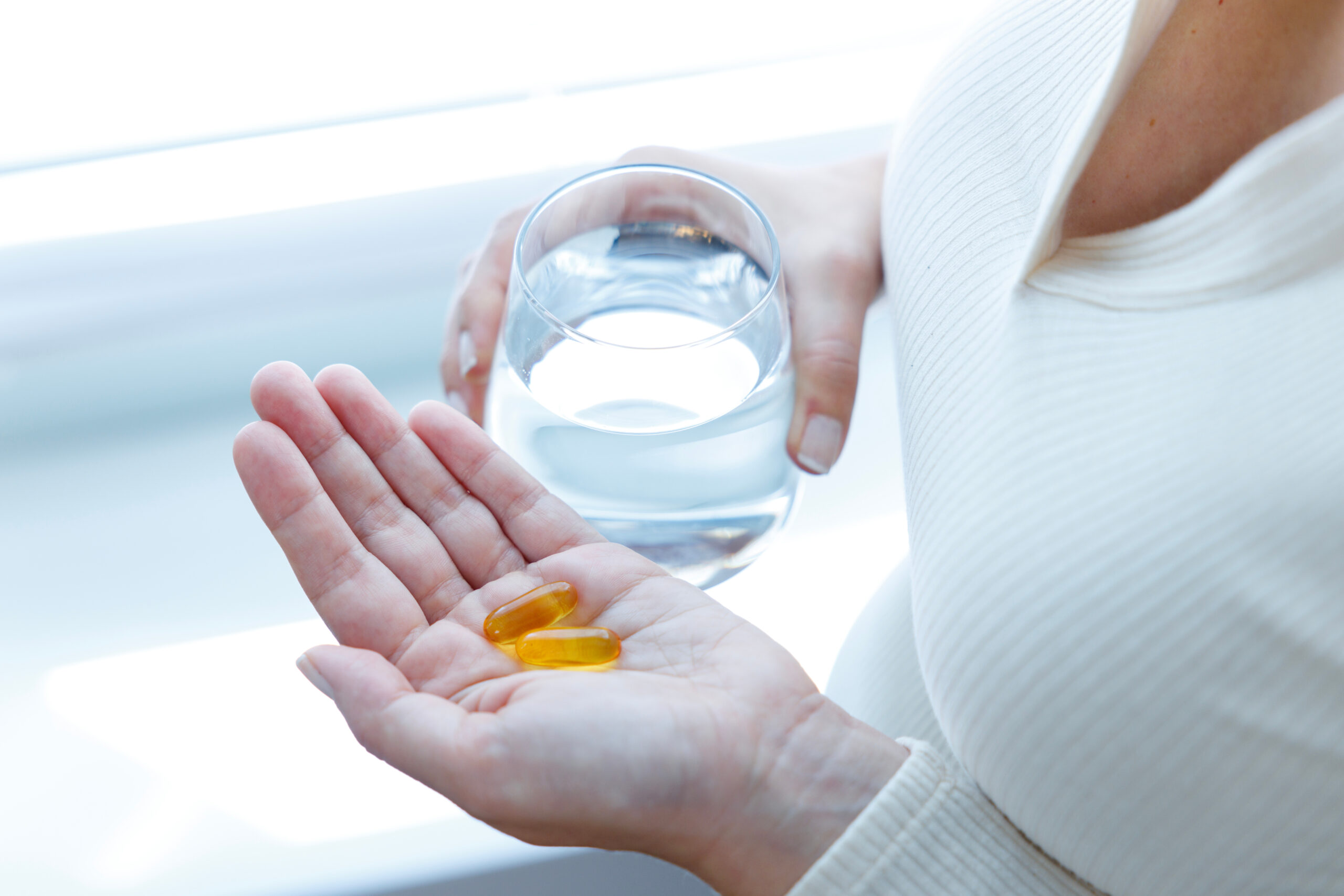 Close up of woman holding vitamin capsules and glass of water. N