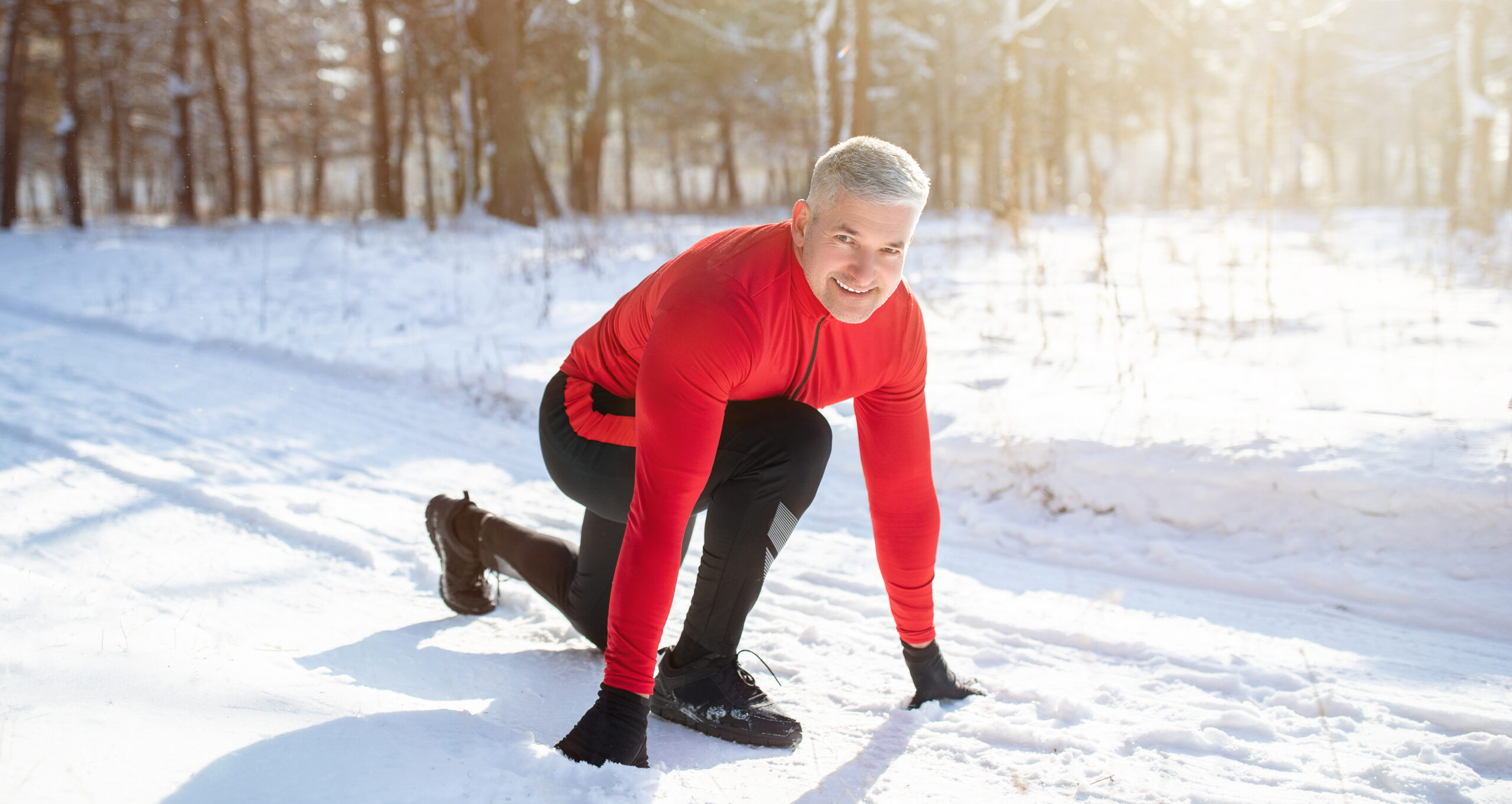 Outdoor winter activities. Mature sportsman getting ready to run marathon on snowy road on cold sunny day, panorama
