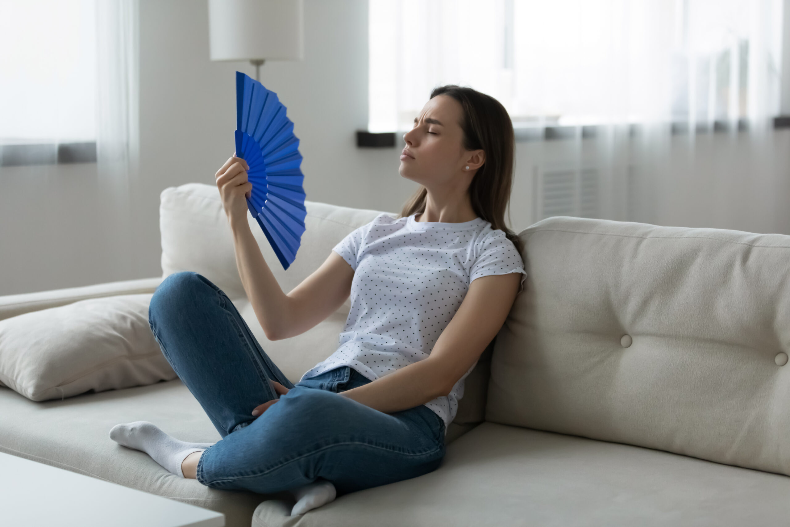 Woman suffers from unbearable hot weather waving fan cooling herself