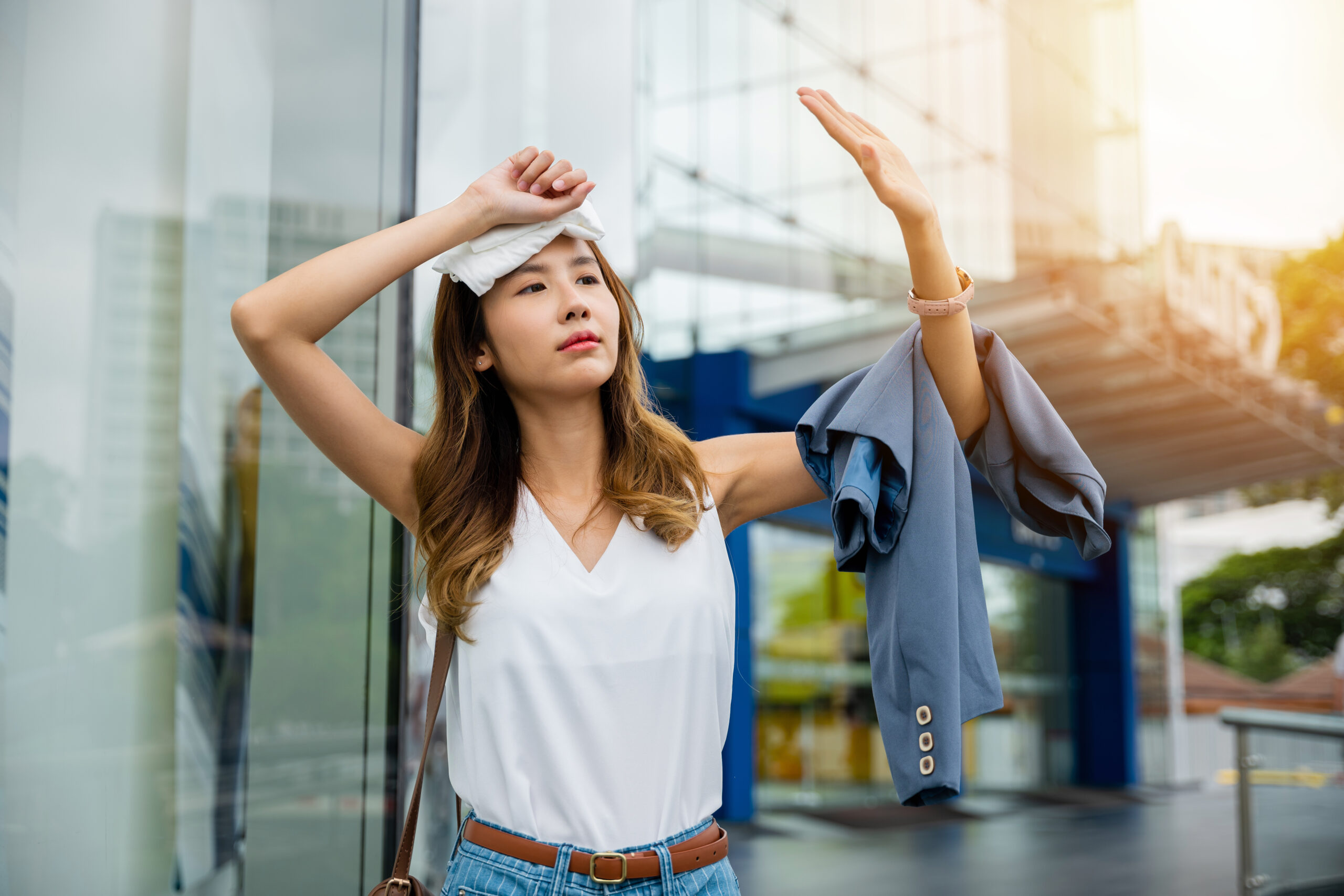 Angry female having sunstroke skin damage from sun UV city air pollution outside on street, Overheating Asian beautiful business woman drying sweat her face with cloth in warm summer day hot weather